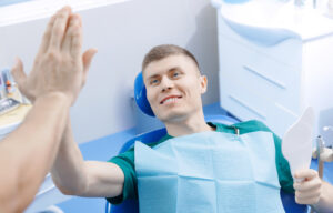 Young happy man client and dentist giving high five to each other in dentistry. Good work is done, concept help overcoming phobias dental.